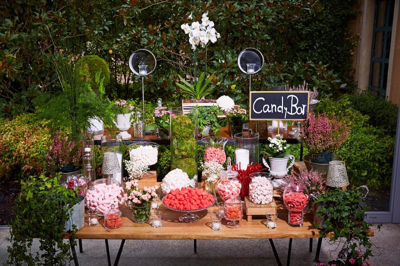 Candy bar entre plantas y flores con recipientes de golosinas